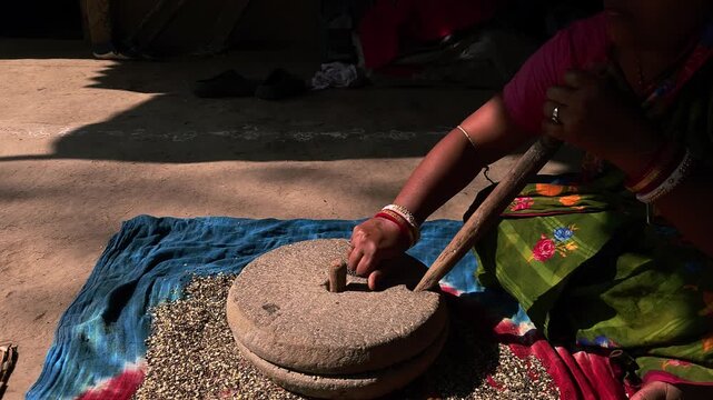 A close-up view of an Indian woman working with a stone quern to grind urad dal highlights traditional village life, sustainable living, and authentic culinary heritage.