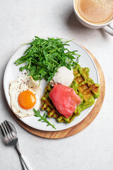 Healthy breakfast with green spinach waffles, salmon, cream cheese, fried egg and salad