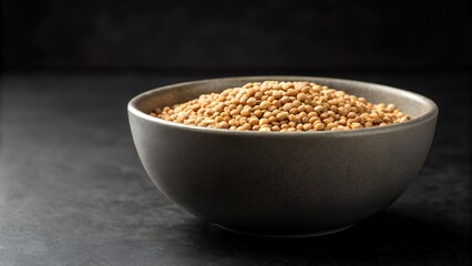 A Bowl of Small Brown Grains Sits on a Dark Textured Surface Under Soft Lighting