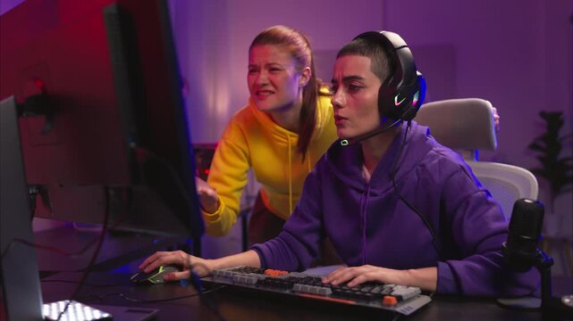 Two woman gamers wearing headsets playing a video game together in a colorful gaming room. They are holding game controllers, interacting with the screen, and enjoying an exciting multiplayer session