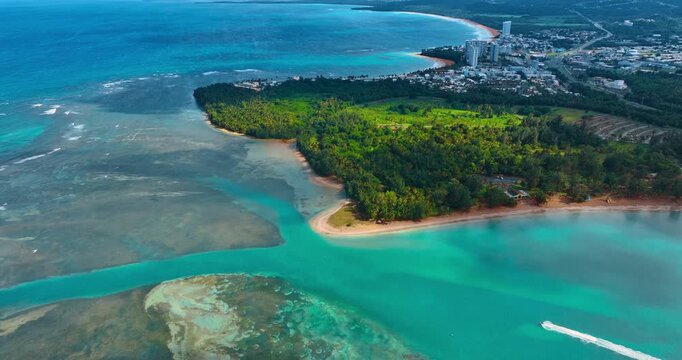 Distancing from green wooded shore surrounded by the turquoise waterscape. A motor boat moves quickly by the water. Aerial view. Puerto Rico.