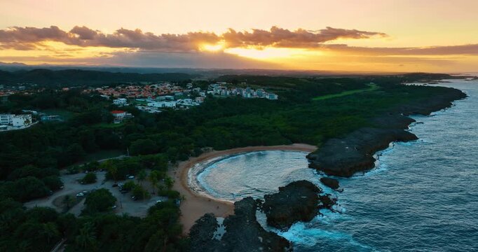 Approaching the beautiful Mar Chiquita beach surrounded in lush greenery. Urban landscape of Manati, Puerto Rico at sunset time at backdrop.