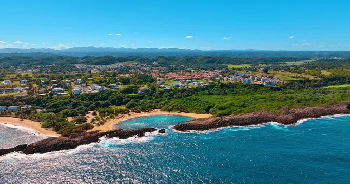 Distancing from brilliant Mar Chiquita beach surrounded by lush greenery. Cityscape of Manati, Puerto Rico at backdrop.