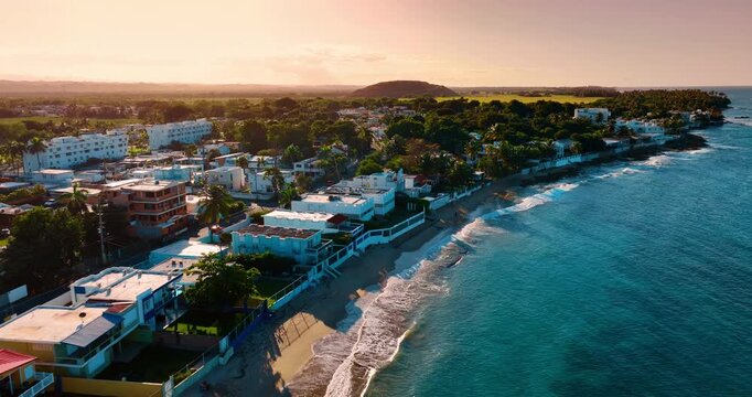 Footage along the sandy beach with villas locating close to the shore. Green nature scenery lit with setting sun at backdrop. Puerto Rico.