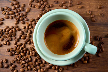 A cup of coffee viewed from above. Coffee beans are scattered around it.       