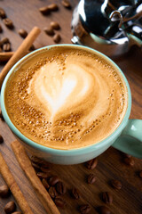 A cup of cappuccino coffee with a foam pattern, top view. Coffee beans and cinnamon sticks are scattered around it.             