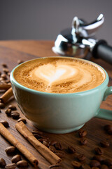 A cup of cappuccino coffee with a foam pattern, top view. Coffee beans and cinnamon sticks are scattered around it.                              