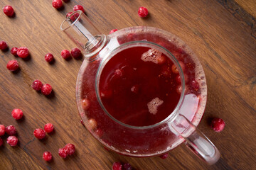Lingonberry tea in a teapot stands on a wooden table, top view