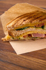 A fresh sandwich with cheese and ham lies on a wooden table