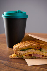 A fresh fast food sandwich with cheese and ham lies on a wooden table with a drink nearby