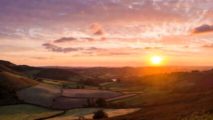 Vibrant sunset casting a warm golden glow over a picturesque rolling landscape with rural fields and distant