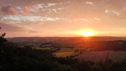 Obraz premium Expansive rural landscape bathed in warm golden light during a vibrant sunset over rolling hills and patchwork
