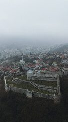 Fototapeta premium Aerial view of Travnik Fortress overlooking the town and surrounding hills, showing historic stone walls, green courtyards and misty mountain landscape from above. Amazing Bosnia and Herzegovina