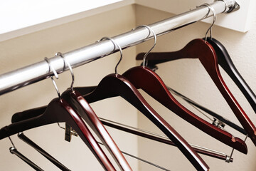 Empty clothes hangers on metal rail. Wooden and black hangers in wardrobe. Closet storage organization concept. Home interior detail. Minimal fashion retail display. Clean simple lifestyle background.