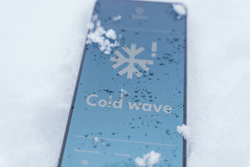 Smartphone lying in snow with cold wave alert on screen, extreme winter weather concept