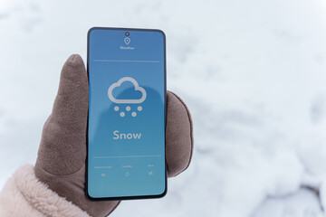 Gloved hand holding smartphone with snow weather forecast on screen in winter outdoors