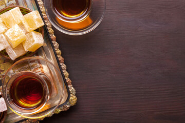 A tray with Turkish delight and tea in traditional glass cups on a dark brown wooden background. Flat lay.