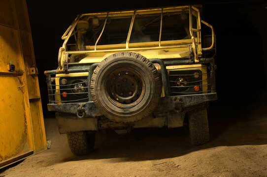 Zakurzony, wytrzymały, ż&oacute;łty samoch&oacute;d terenowy stoi nocą przy ż&oacute;łtej bramie garażowej, prezentując przedni grill, koło zapasowe i solidny zderzak.