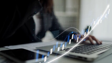 A business professional focuses on a laptop while analyzing financial data represented by an overlay graph, showcasing growth trends in a modern workspace. Copula