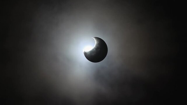 Partial solar eclipse showing a crescent of the sun peeking through dark clouds moon celestial