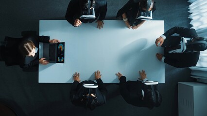 Top down aerial view of diverse data analysts wearing VR headset and stand around table while using hand gestures to manipulate the data streamed live from executive manager's laptop. Directorate.