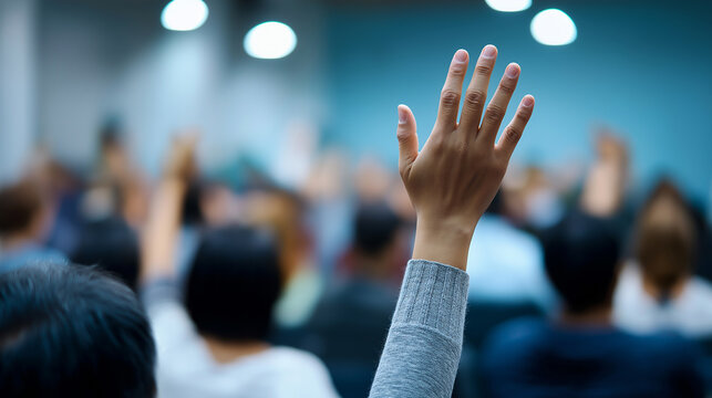 Audience members raising hands during a conference or seminar, representing participation and engagement.

