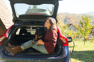 Woman with her dog sitts into trunk of electric car