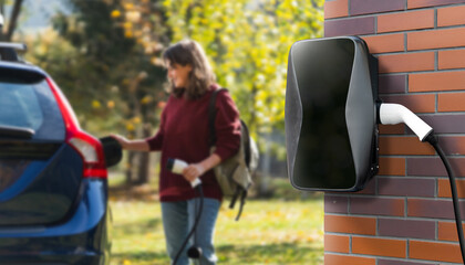 Woman traveler with backpack next to charging electric car