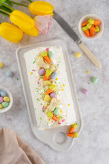 Easter carrot roll cake with cream cheese frosting, decorated chocolate eggs, jellied carrots and sugar sprinkles on top. Traditional carrot roll cake on a concrete background. Easter festive dessert.