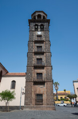 The bell tower of the Church of Nuestra Se&ntilde;ora de la Concepci&oacute;n rises against a clear blue sky in La Laguna, Tenerife, Spain, showcasing its historic stone architecture and clock faces