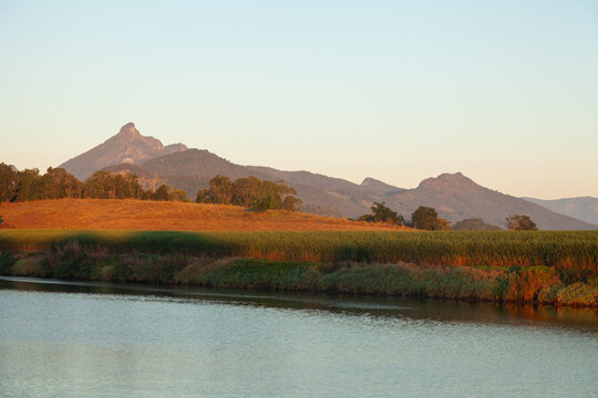 Sunrise light illuminating Mount Warning and surrounding farmland with cultivated cane fields beside a calm river, agricultural landscape farming traditions, Murwillumbah, New South Wales,  Australia.
