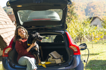 Woman with her dog sitts into trunk of electric car