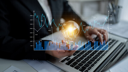 A business professional is analyzing financial data while holding a glowing light bulb,...