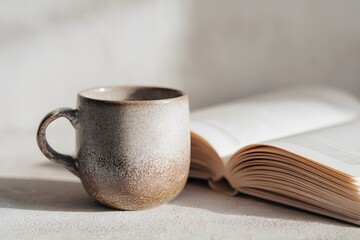Cozy ceramic mug beside an open book on a textured surface, embodying the essence of slow living and relaxation, perfect for a day of slowness and mindfulness