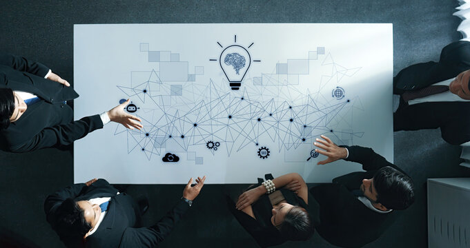 A diverse group of business professionals engages in a collaborative meeting around a modern table with technology graphics, emphasizing innovation and strategic planning. Trope - Powered by Adobe