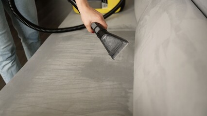 Cleaning service specialist professionally removing dirt from a sofa. Female hand using a wet vacuum cleaner for furniture deep cleaning