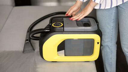 Unrecognizable woman assembling a modern yellow spot cleaning vacuum. Housewife preparing a professional cordless deep cleaner for home use