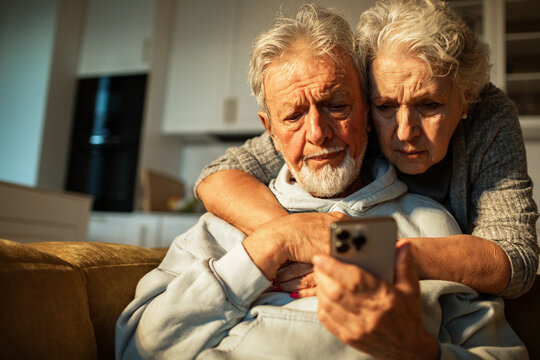 Senior couple looking concerned at smartphone on sofa at home