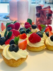 mini fruit tartlets with cream and fresh berries; elegant mini tartlets filled with creamy frosting and topped with fresh raspberries, blueberries, strawberries, and mint leaves