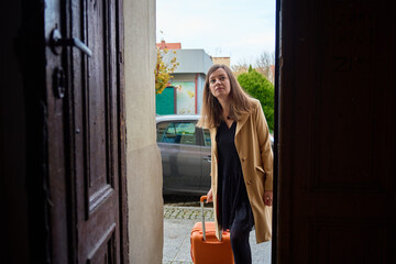 Woman traveler with suitcase entering building through open door