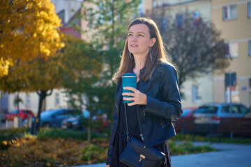 Woman holding reusable coffee cup on city street