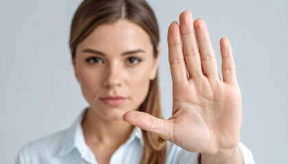 Close-up portrait of a serious young woman holding her palm outward in a stop gesture against a neutral background with soft, natural lighting