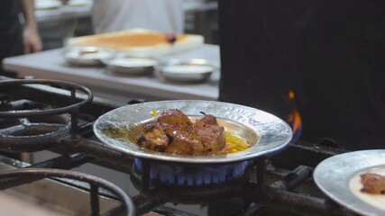 Close-up 10-bit slow motion of a chef pouring hot clarified butter over grilled cubed meat (Kuşbaşı) in a traditional metal plate. The oil creates a cinematic flame effect. 4K quality.