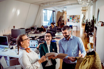 Adult coworkers laughing over fashion designs in a modern studio