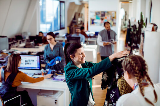 Young adult women smiling while reviewing clothing in a creative office