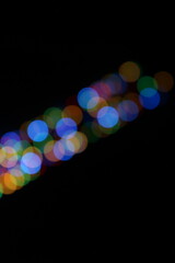 A bokeh effect photograph of multicolour circle fairy lights against a black background.