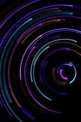 A long exposure photograph. Light painting photography; vibrant multicolour fairy lights in a circle swirl pattern against a black background