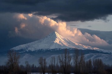 Snow-covered mountain peak under cloudy sky with light