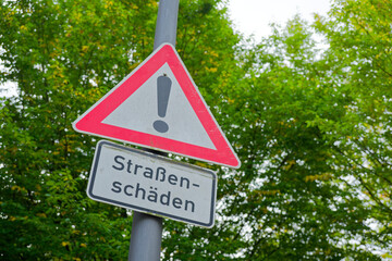 Warning road damage sign with exclamation symbol on street pole in city © Holger