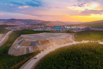 Aerial view of open pit mine at sunset in forested landscape, big yellow truck moving on road